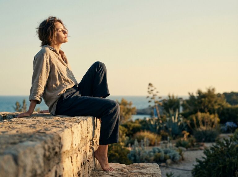 Woman sitting on stone wall in morning coastal light