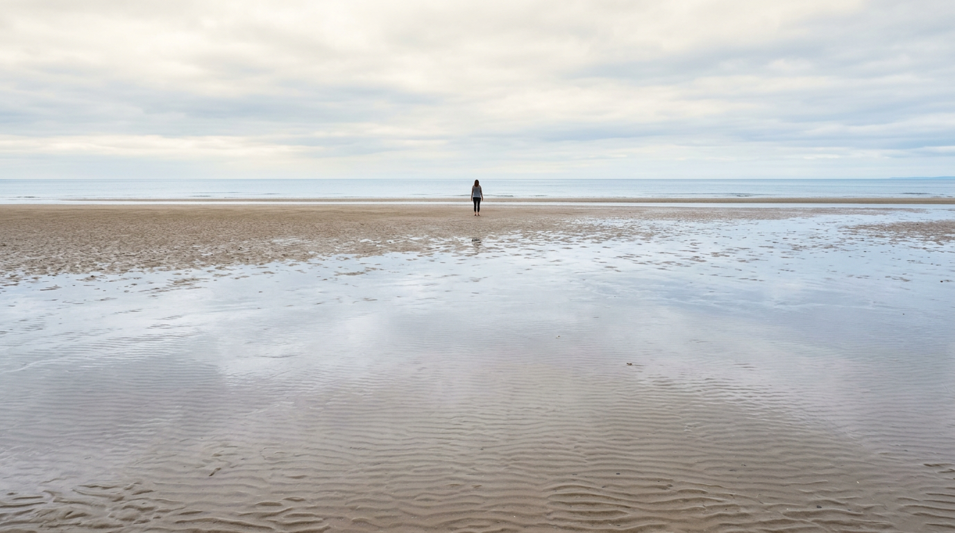 Woman standing on wide exposed beach at low tide under an overcast sky